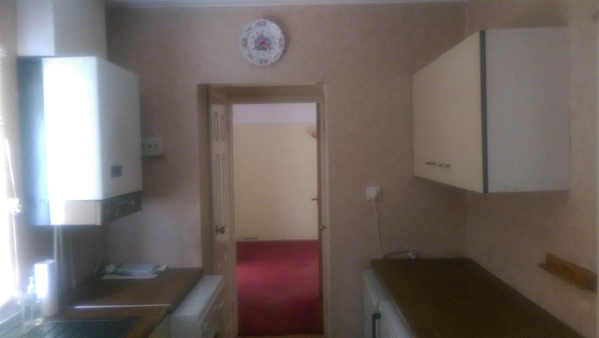 Before — original narrow galley kitchen with cream units, dark worktops and a boiler on the wall